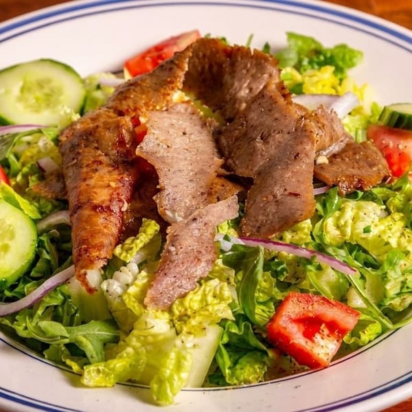 A fresh salad with sliced meat, lettuce, cucumbers, tomatoes, and red onions on a white plate.