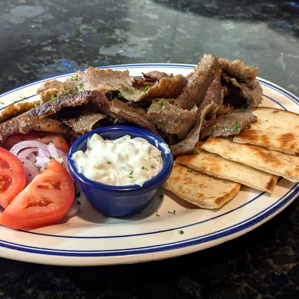 A gyro plate with sliced gyro meat, warm pita wedges, tzatziki, sliced tomatoes, and red onion.