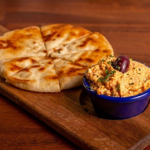 Pita bread cut into wedges next to a blue bowl of hummus topped with an olive.
