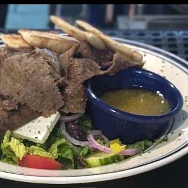 A gyro platter with seasoned gyro meat, warm pita wedges, tzatziki, dipping sauce, and a Greek salad.