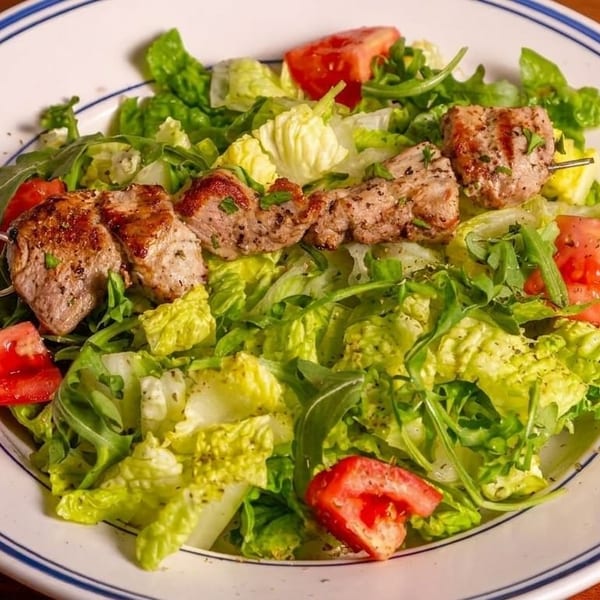 Grilled meat skewers on a bed of fresh green lettuce and tomato salad.