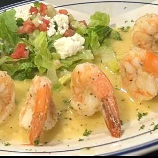 Sauteed shrimp in a lemon-butter sauce served with a fresh Greek salad on a white plate.